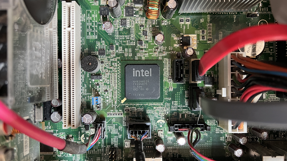Ảnh cận cảnh bên trong máy tính để bàn hiển thị bo mạch chủ màu xanh lá cây với chipset Intel, khe cắm mở rộng, tụ điện, tản nhiệt, cáp nguồn và kết nối dữ liệu được gắn trên bảng mạch.