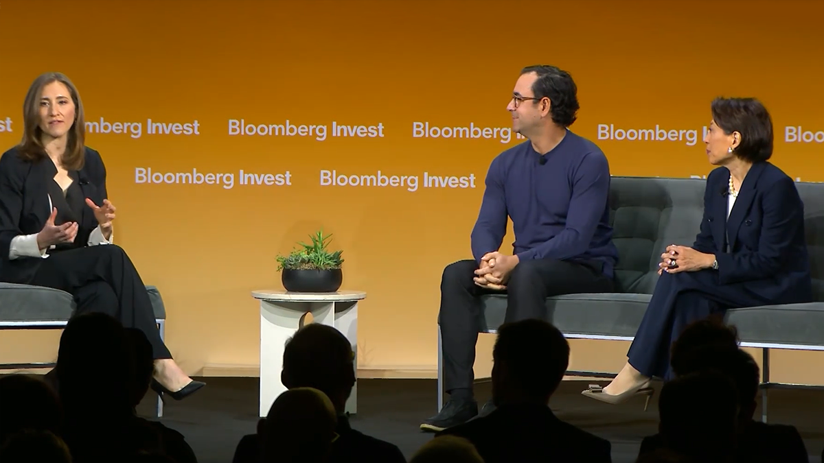 Thảo luận nhóm tại Bloomberg Invest có ba diễn giả ngồi trên sân khấu trước phông nền màu cam có biểu tượng Bloomberg thảo luận về tín dụng tư nhân và khả năng tiếp cận thị trường bán lẻ với bóng của khán giả ở phía trước.